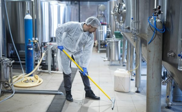 Professional industrial cleaner in protective uniform cleaning floor of food processing plant.